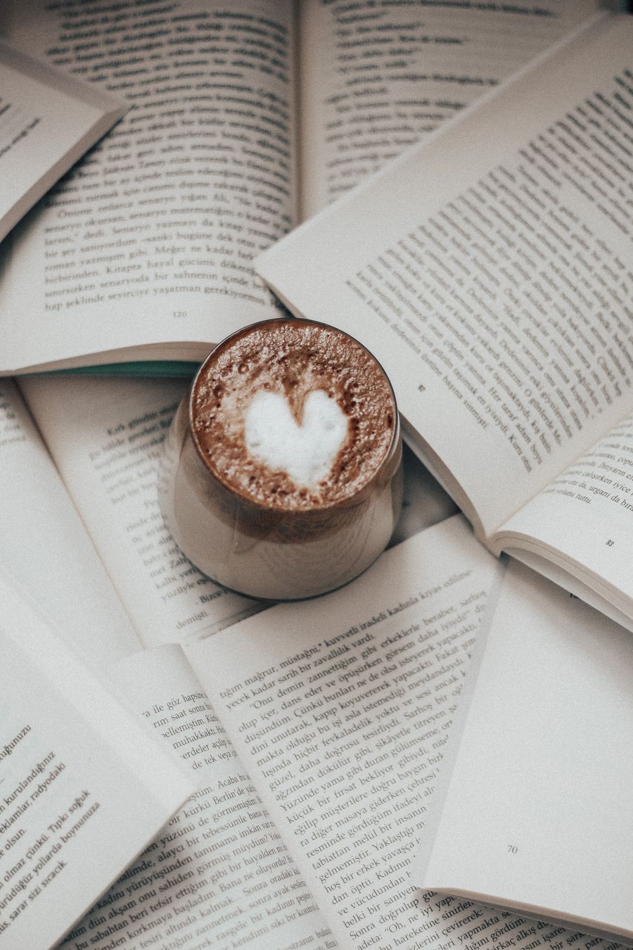 Ein einzelnes, aufgeschlagenes Buch auf einem Tisch im weichen Nachmittagslicht, daneben eine Tasse Kaffee.